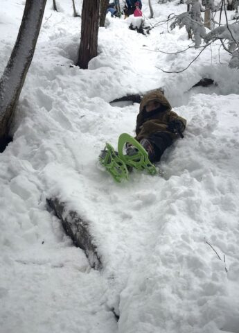 お尻で雪山を滑り降りる子ども
