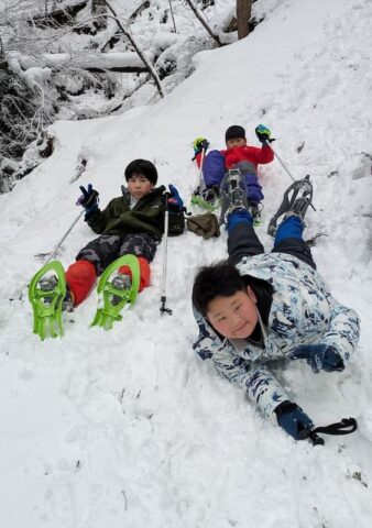 スノーシューを履いて雪山で休憩中の子どもたち